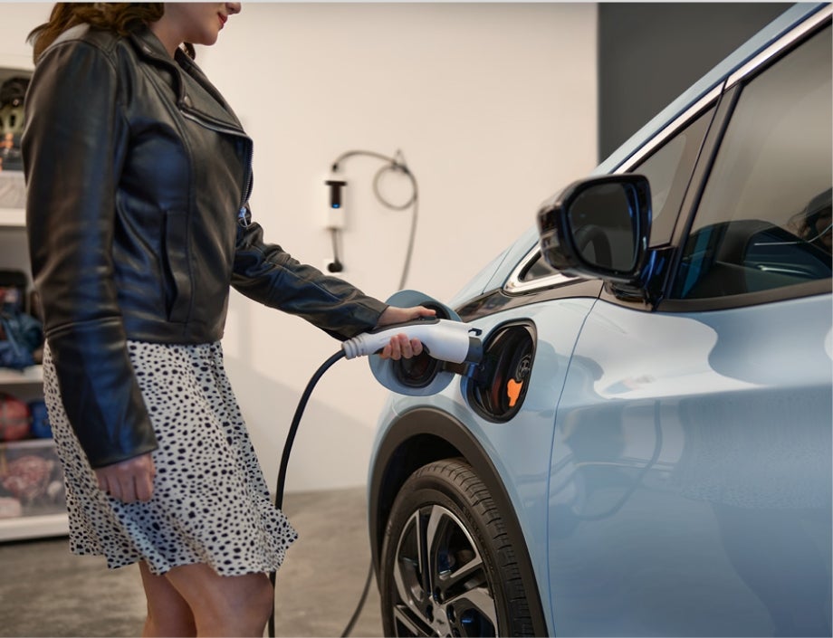 A Woman Standing in Her Garage Plugging in the Charger for her Chevrolet Bolt EV